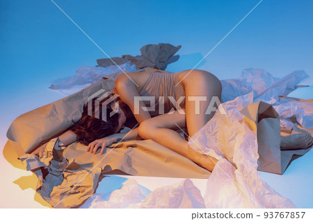 Conceptual portrait of young tender girl in lingerie lying on floor with cloth, paper sheets over light blue background. Mental health, art, creation 93767857