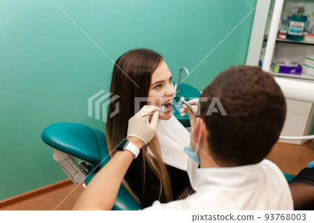 Dentist with a drill and a mirror is treating a patient teeth.. 93768003