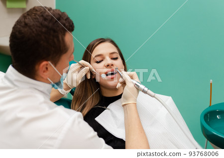 Dentist performs professional polishing of tooth enamel for woman patient.. 93768006