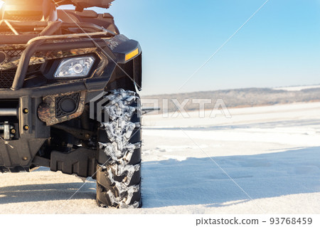 Front POV close-up detail view of quad bike offroad vehicle parked in snowdrift track on sunny snowy cold winter morning against clear blue sky. ATV adventure extreme sport. Nature country tour drive Front POV close-up detail view of quad bike offroad vehicle parked in snowdrift track on sunny snowy cold winter morning against clear blue sky. ATV adventure extreme sport. Nature country tour drive 93768459