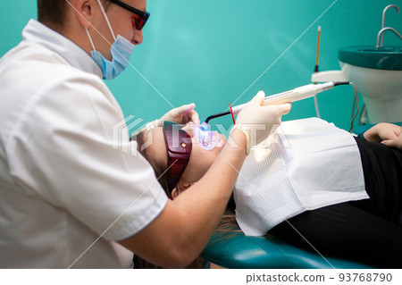 Dentist using whitening ultraviolet lamp on her teeth. Young girl patient at the dental clinic lies in uv glasses on the dentist's chair.. 93768790