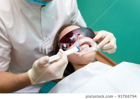 Dentist applies a tooth whitening gel with a syringe. Girl undergoes a teeth whitening procedure in a dental clinic.. 93768794
