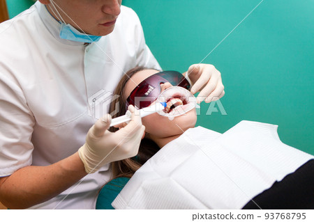 Dentist applies a tooth whitening gel with a syringe. Girl undergoes a teeth whitening procedure in a dental clinic.. 93768795