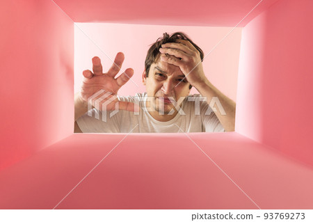 Young man looking inside box with unpleasant face. Emotions of disgustion. Young man looking inside box with unpleasant face. Emotions of disgustion. 93769273