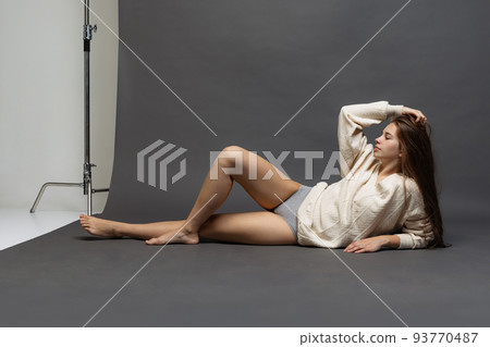 Studio shot of charming girl with long glossy hair wearing sweater and underwear isolated over gray background. Studio shot of charming girl with long glossy hair wearing sweater and underwear isolated over gray background. 93770487