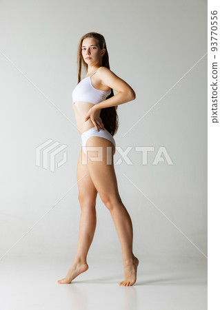 One young girl with long glossy hair wearing white underwear isolated over gray background. Wellness, wellbeing, aesthetic cosmetology concept. 93770556