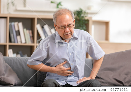 Senior men holding his stomach feeling pain while sitting on the sofa at home. Asian man having stomachache with isolated gastric. Senior suffering from digestion problem or acid reflux. 93771911