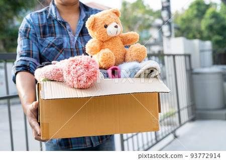 Holding clothing donation box with used clothes and doll at home to support help for poor people in the world. 93772914