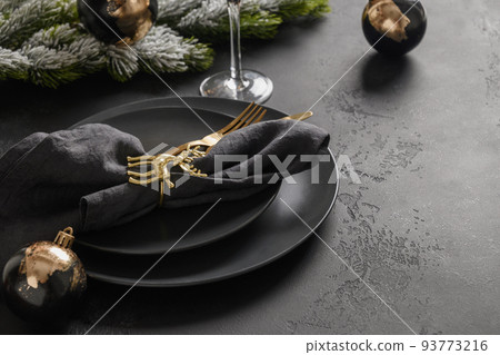 Christmas table setting with black plate and golden decorations on black background. 93773216