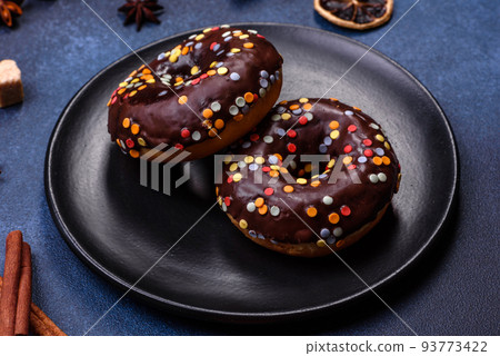 Pastries concept. Donuts with chocolate glaze with sprinkles, on a dark concrete table Pastries concept. Donuts with chocolate glaze with sprinkles, on a dark concrete table 93773422
