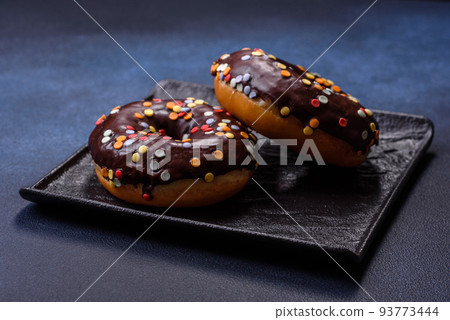Pastries concept. Donuts with chocolate glaze with sprinkles, on a dark concrete table Pastries concept. Donuts with chocolate glaze with sprinkles, on a dark concrete table 93773444