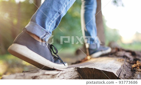 the boy is playing in the forest park. close-up child's legs walking on a log of a fallen tree. happy family childhood dream concept. a child in sneakers walks on fallen tree in park 93773686