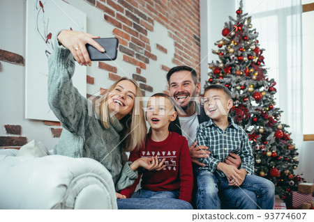 Beautiful happy married couple with two children using smart phone talking to friends or family congratulates Merry Christmas by video call conference app. Modern technology New Year 2022 congrats. Beautiful happy married couple with two children using smart phone talking to friends or family congratulates Merry Christmas by video call conference app. Modern technology New Year 2022 congrats. 93774607