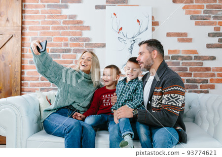 Young family having fun talking on a video call using a mobile phone, rejoicing and smiling, husband wife and your guys brothers greet friends with New Year and Christmas holidays 93774621
