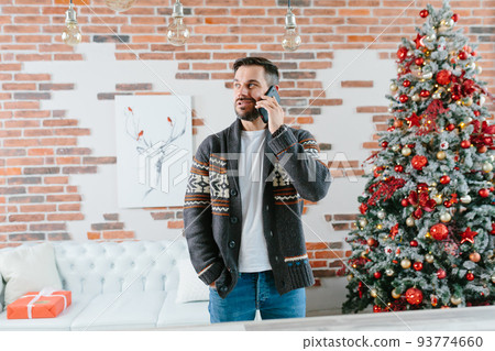Before New Year's Eve, a young man sits on a sofa and talks on a mobile phone with friends 93774660