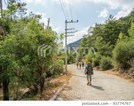 Tourists with backpacks walk to Goynuk Canyon. Cobble way along mountain slopes in Beydaglari Coastal National Park. Turkey. 93774767