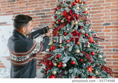 A man with a beard himself decorates a Christmas tree for the New Year and Christmas holidays A man with a beard himself decorates a Christmas tree for the New Year and Christmas holidays 93774986