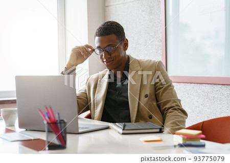 Busy african businessman in glasses working on laptop while sitting in modern coworking Busy african businessman in glasses working on laptop while sitting in modern coworking 93775079