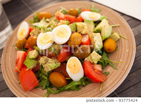dish of fresh vegetables arugula, avocado, cherry tomatoes with olives and quail eggs on dining table 93775424