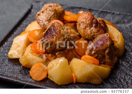 Beef meat and vegetables stew on a black plate with roasted potatoes Beef meat and vegetables stew on a black plate with roasted potatoes 93776157