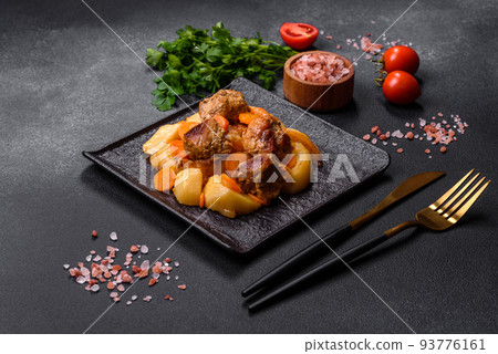 Beef meat and vegetables stew on a black plate with roasted potatoes 93776161