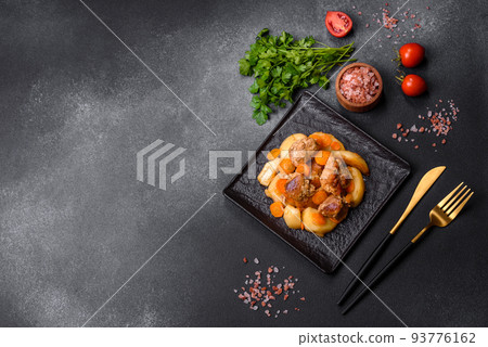 Beef meat and vegetables stew on a black plate with roasted potatoes 93776162