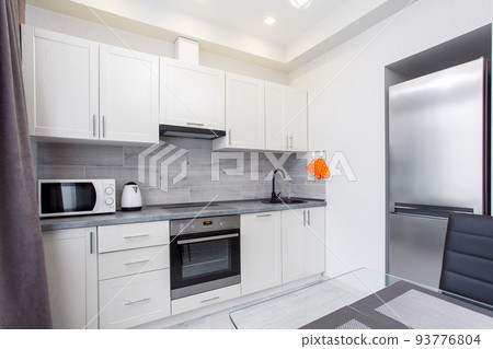 Clean kitchen in a small cozy contemporary studio apartment. Table and chairs in the foreground. Built in household appliance 93776804