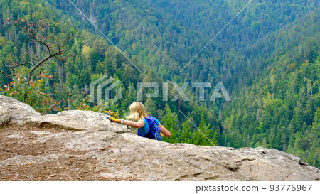 The woman was climbing a stone cliff. A view of the most beautiful mountains in a panoramic scene. View from Tomasovsky Vyhlad in Slovak Paradise National Park. Blue haze in the air 93776967
