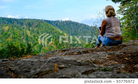 A woman enjoys the view of nature, holding a mobile phone. A view of the most beautiful mountains in a panoramic scene. View from Tomasovsky Vyhlad in Slovak Paradise National Park. Blue haze in the 93776972