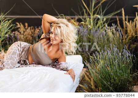 an attractive middle-aged blonde woman in home clothes in bed among lavender. an attractive middle-aged blonde woman in home clothes in bed among lavender. 93778044