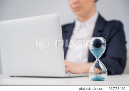 Business woman keeps track of time on an hourglass while working. 93778461