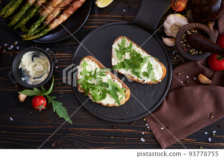Tasty breakfast - toasts with cream cheese and Asparagus wrapped with bacon and spices on a plate 93778755