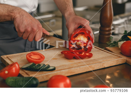 Busy chef cutting red pepper and cucumbers on a board for making salad in modern restaurant kitchen Busy chef cutting red pepper and cucumbers on a board for making salad in modern restaurant kitchen 93779106