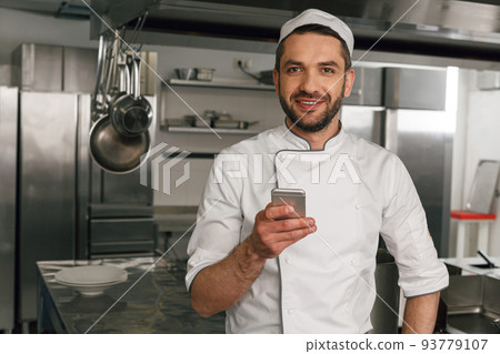 Chef cook using smart phone at the restaurant kitchen and looking camera 93779107