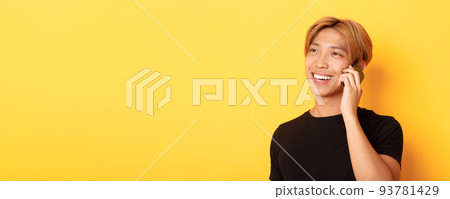 Close-up of handsome carefree asian guy with fair hair, talking on mobile phone and smiling happy, standing yellow background Close-up of handsome carefree asian guy with fair hair, talking on mobile phone and smiling happy, standing yellow background 93781429