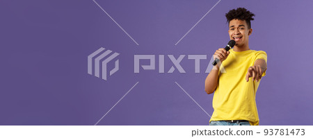 This song is for you. Portrait of romantic carefree hispanic man singing karaoke, pointing at camera as dedicate his performance, holding microphone, standing purple background 93781473