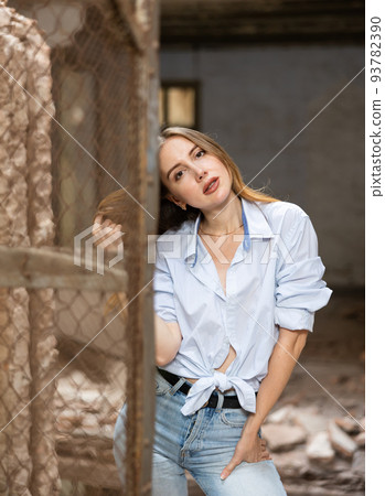 Young woman in knotted shirt posing near steel mesh fencing inside destroyed building 93782390