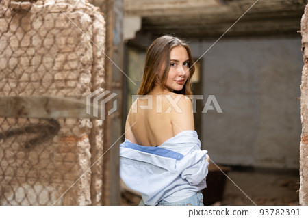 Rear view of young woman in shirt with bared back, standing in dilapidated abandoned house 93782391