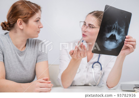 A woman doctor and a patient at the reception are discussing an x-ray of the sinuses. 93782916