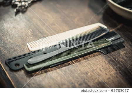 Arrangement Professional hairdressing barberian Barbershop tools accessories for hair simple plastic white black green combs lying on wood table background retro barber shop salon. Vintage toned photo Arrangement Professional hairdressing barberian Barbershop tools accessories for hair simple plastic white black green combs lying on wood table background retro barber shop salon. Vintage toned photo 93785077