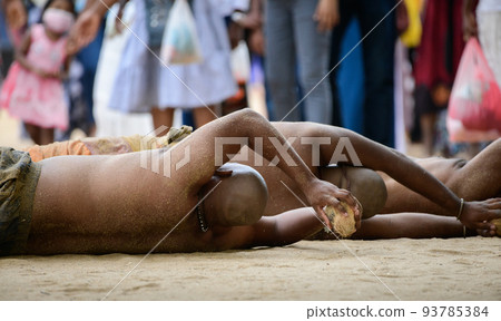 A Group of men rolls barely clads on hot sands near the temple to show their faith and dedication to God Kataragama, holding a coconut in both hands and rolling around the temple. 93785384