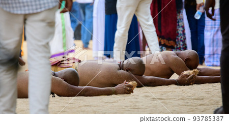A Group of men rolls barely clads on hot sands near the temple to show their faith and dedication to God Kataragama, holding a coconut in both hands and rolling around the temple. 93785387