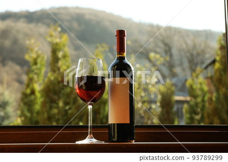 Glass and bottle of wine stands on wooden windowsill 93789299