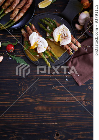 Tasty breakfast - toasts with cream cheese, poached eggs and Asparagus wrapped with bacon and spices on a plate 93791115