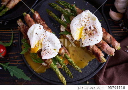 Tasty breakfast - toasts with cream cheese, poached eggs and Asparagus wrapped with bacon and spices on a plate Tasty breakfast - toasts with cream cheese, poached eggs and Asparagus wrapped with bacon and spices on a plate 93791116