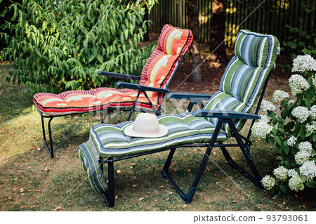 Two soft sun loungers with straw hat in inner courtyard. Two empty sun beds in a sunny garden for relaxation. Two soft sun loungers with straw hat in inner courtyard. Two empty sun beds in a sunny garden for relaxation. 93793061