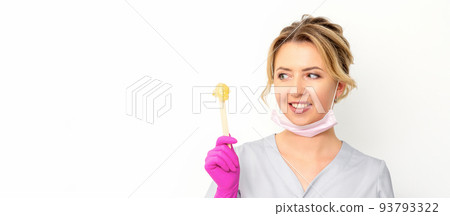 The master of sugar hair removal holds liquid yellow sugar paste, wax for depilation on a wooden stick on a white background The master of sugar hair removal holds liquid yellow sugar paste, wax for depilation on a wooden stick on a white background 93793322