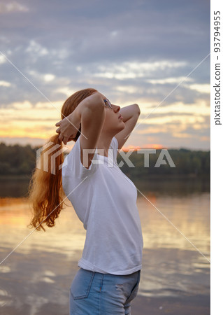 Young woman by the lake at sunset stands in profile 93794955