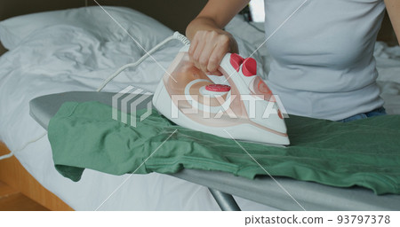 Woman iron clothes with iron on ironing board Woman iron clothes with iron on ironing board 93797378