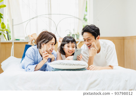 一家人躺在床上看智能手機 93798012